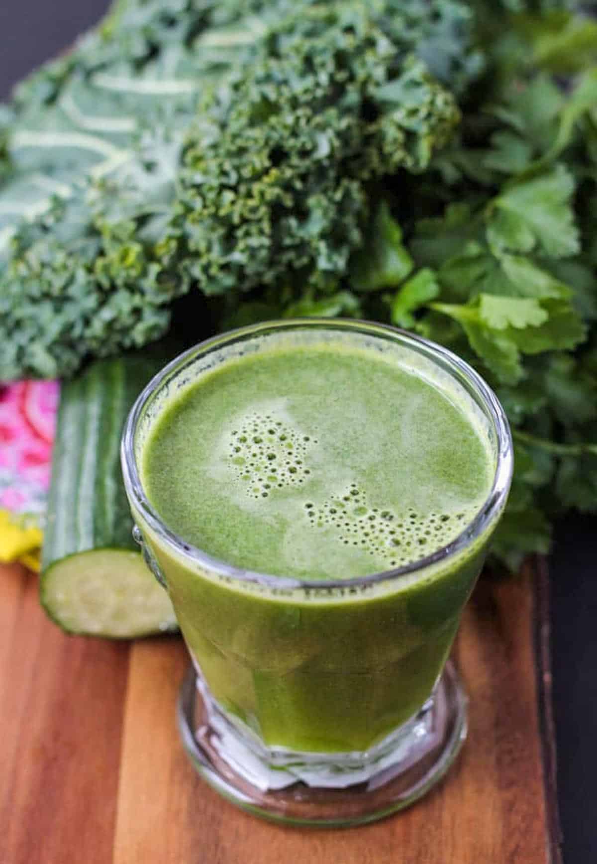 Glass of green juice surrounded by fresh produce.
