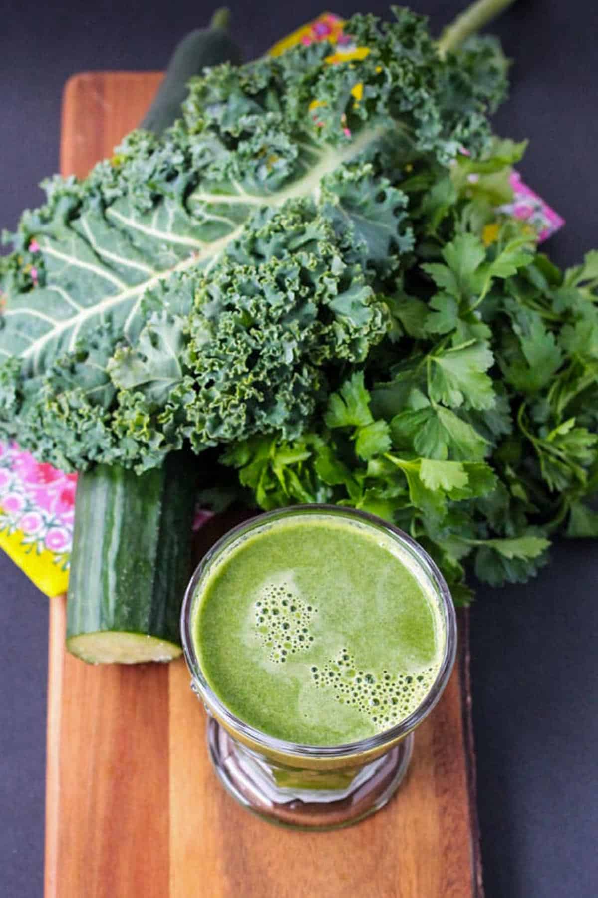 Glass of green juice next to lots of fresh green vegetables.