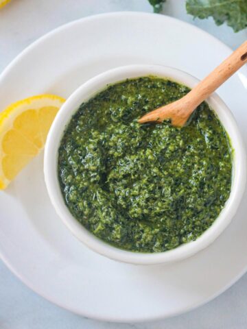 Small wooden spoon in a bowl of kale walnut pesto.