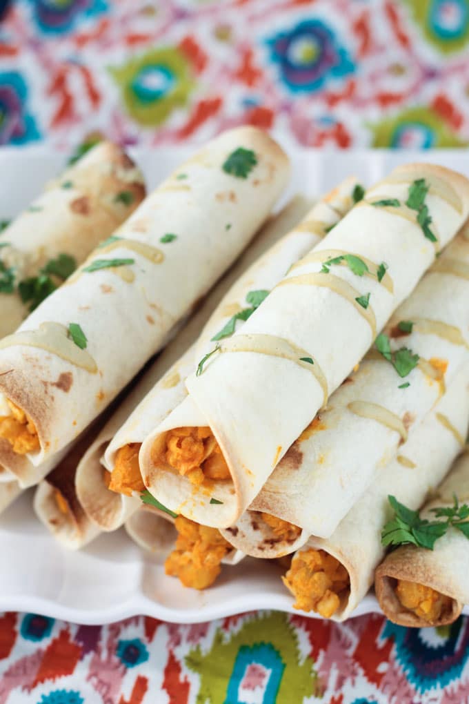 Close up shot of Baked Vegan Taquitos drizzled with dairy free ranch dressing and sprinkled with fresh parsley.