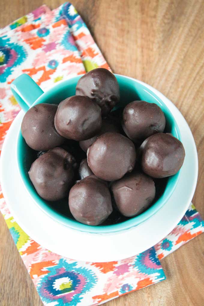 Overhead view of a blue bowl of Cherry Chocolate Truffles on a white plate. Brightly colored patterned dish towel underneath.