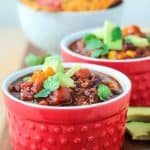Two bowls of black bean chili in red bowls.