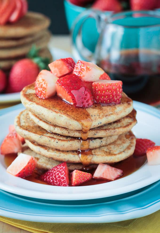 Stack of Lemon Poppyseed Pancakes topped with fresh chopped strawberries and a drizzle of maple syrup.