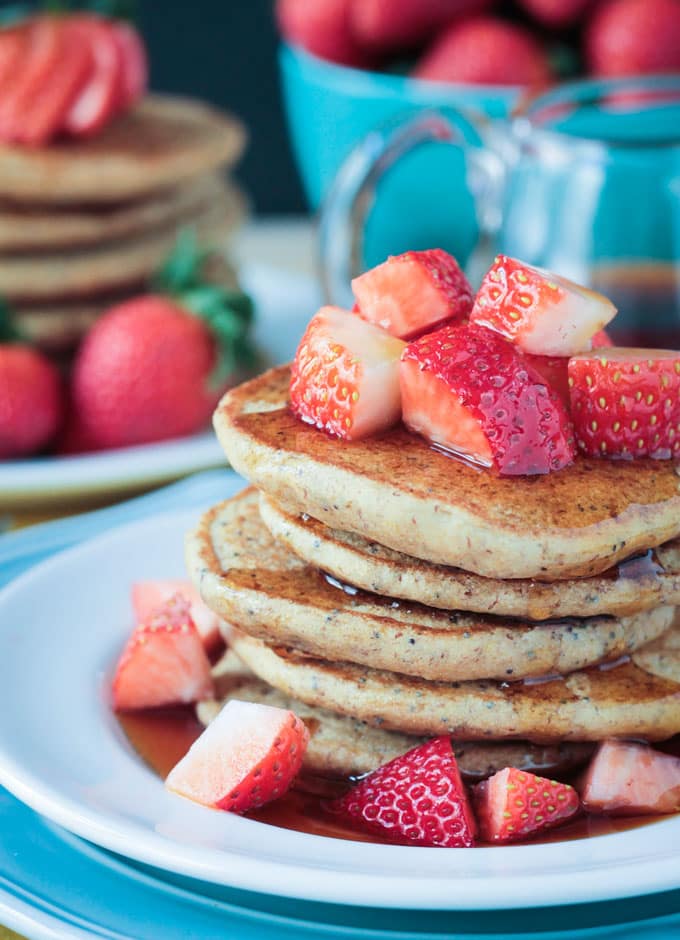 Close up of a stack of Lemon Poppyseed Pancakes topped with chopped strawberries and maple syrup.