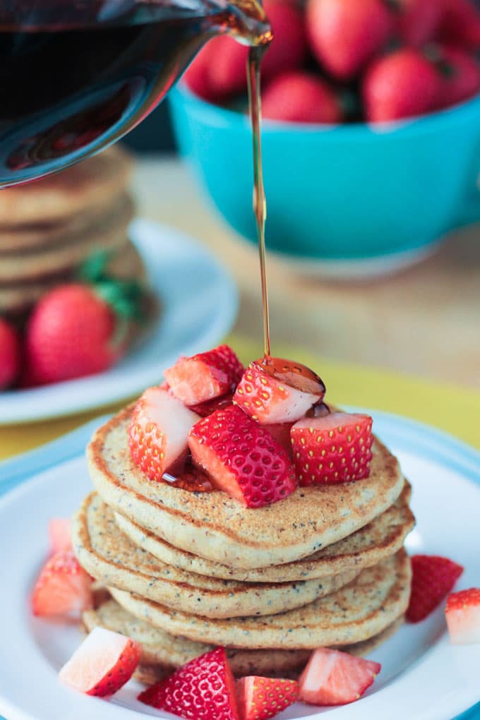 A drizzle of maple syrup being poured over a stack of Lemon Poppyseed Pancakes