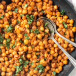 Close up of seasoned chickpeas on a spoon in a skillet.
