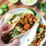 Hand holding one taco above a dinner plate.