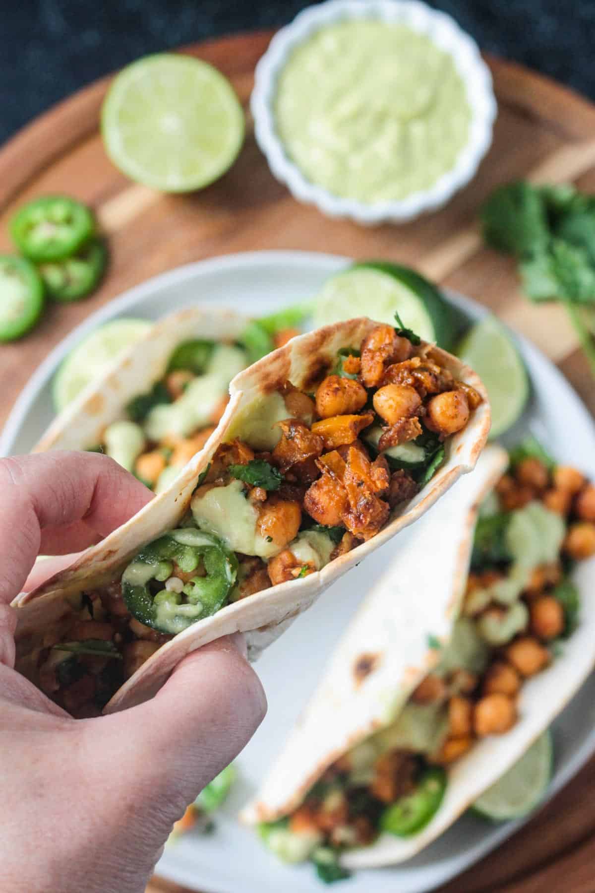 Hand holding one taco above a dinner plate.