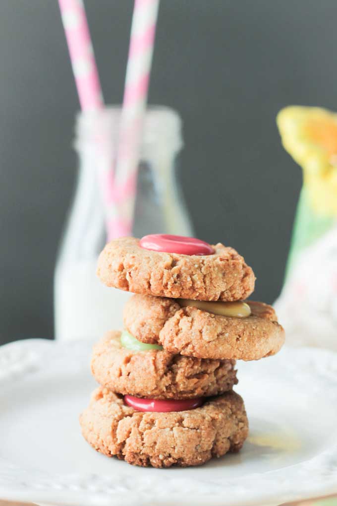 Stack of 4 pastel Gluten Free Thumbprint Cookies with a glass of milk and two pink straws behind.