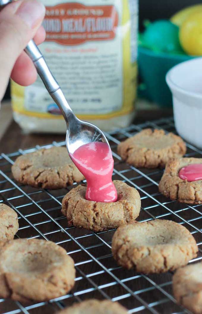 Pink icing being spooned into gluten free thumbprint cookies