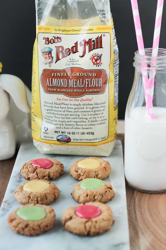 Gluten Free Thumbprint Cookies in front of a bag of Bob's Red Mill Almond Flour and a glass of milk.