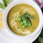Bowl of creamy green vegetable soup garnished with peas & a sprig of dill.