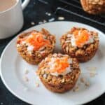 Three carrot cake baked oats muffins on a white plate next to a cup of coffee.