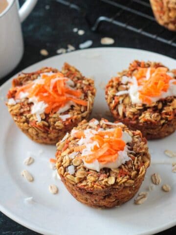 Three carrot cake baked oats muffins on a white plate next to a cup of coffee.