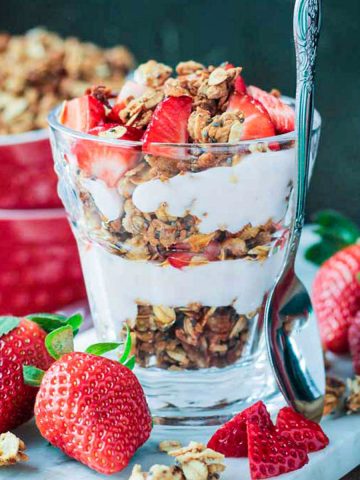 Coconut Chia Granola layered with dairy free yogurt and fresh strawberries in a parfait glass.