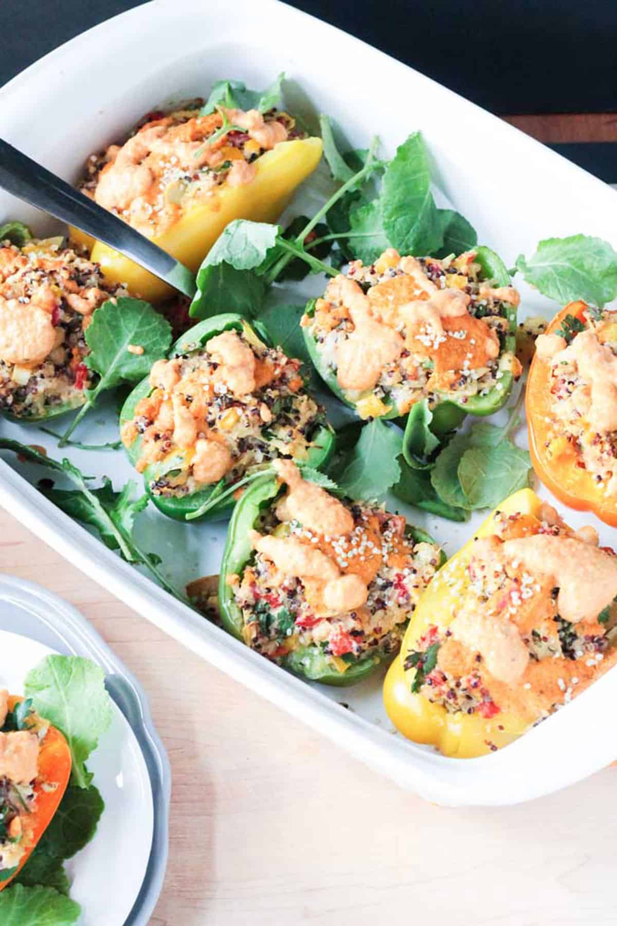 White casserole dish of stuffed peppers on top of fresh baby kale.