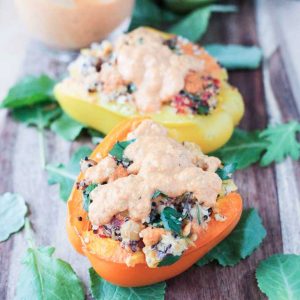 Two quinoa stuffed peppers with red pepper sauce drizzled on top.