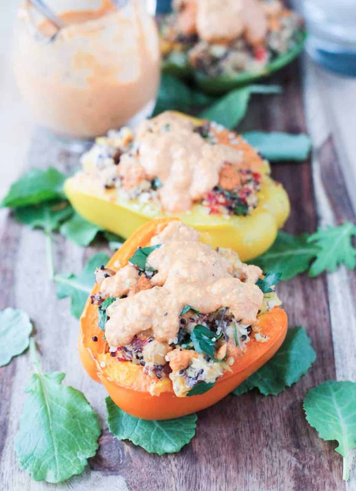 Two quinoa stuffed peppers with red pepper sauce drizzled on top.
