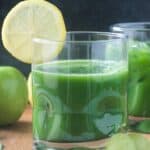 Green juice in a glass with a lemon slice on the rim.