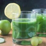 Green juice in a glass with a lemon slice on the rim.