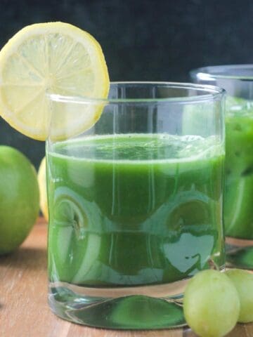 Green juice in a glass with a lemon slice on the rim.