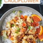 Vegan orange cauliflower in a sticky sauce with diced peppers over rice in a gray flat bowl.