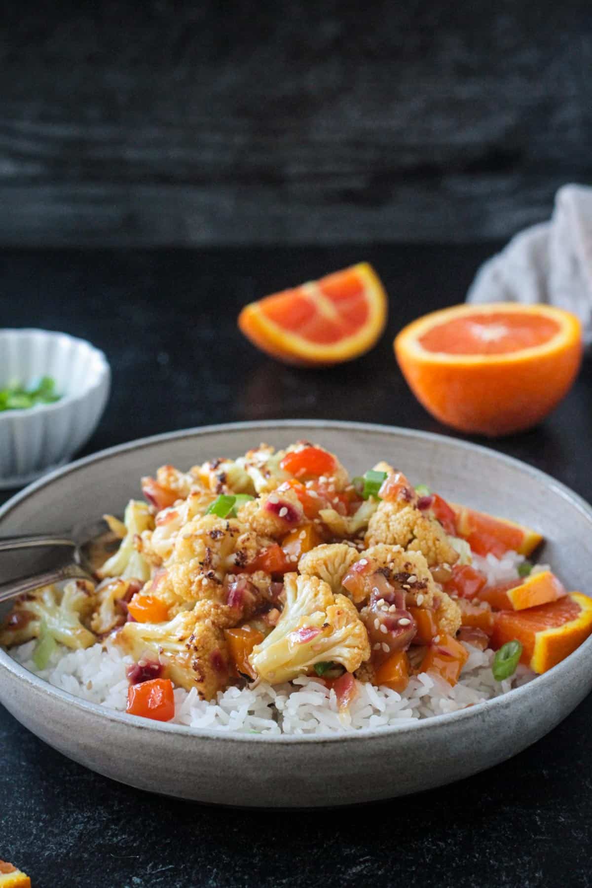 Rice topped with vegan orange cauliflower in a gray flat bowl.