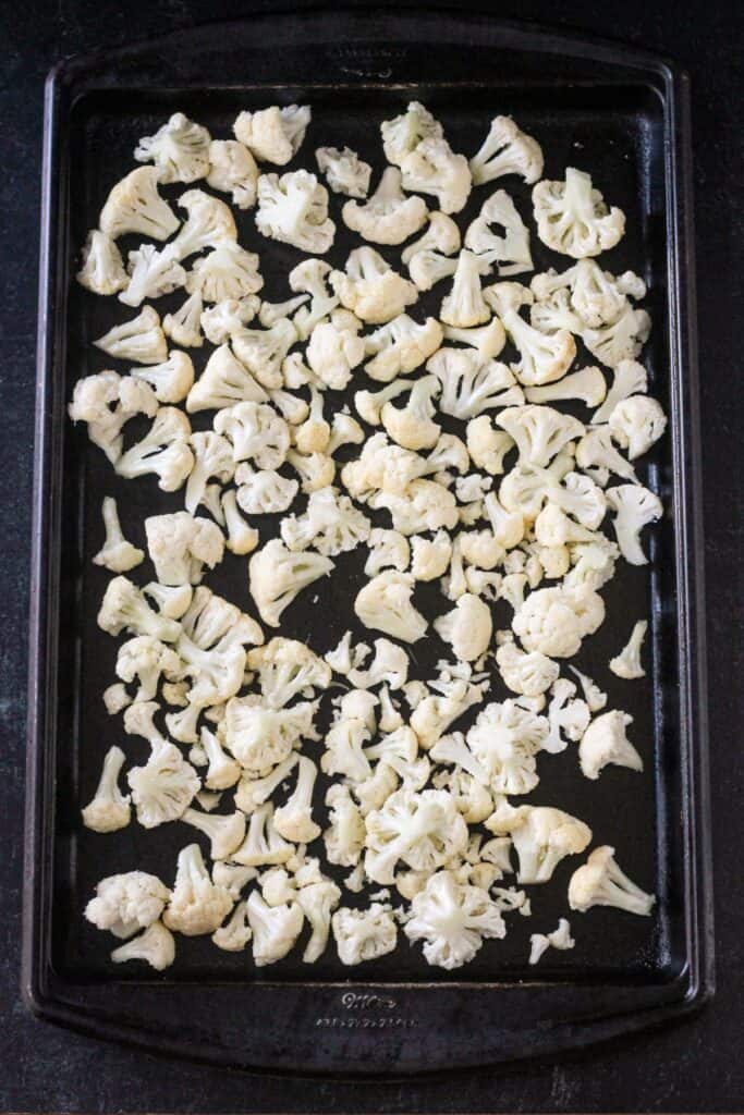 Raw cauliflower florets spread out on a rimmed baking sheet.