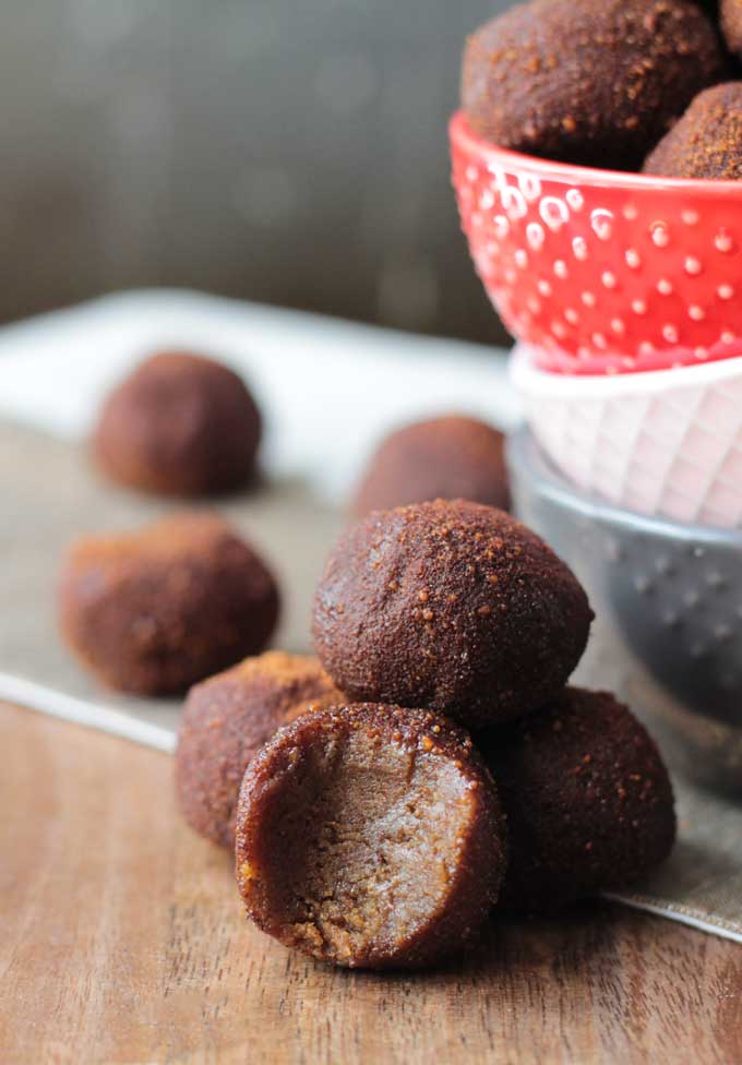4 Cinnamon Chickpea Dairy Free Truffles in a pile. Front one has a bite taken out. More truffles in a bowl in the background.