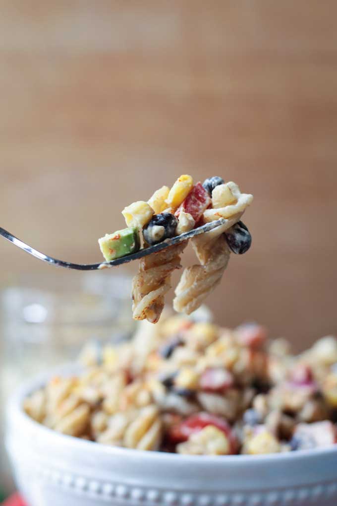 One bite of southwest black bean pasta salad on a metal fork being lifted out of a bowl.