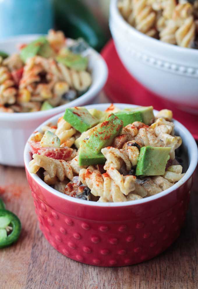Southwest Black Bean Pasta Salad, topped with lots of diced avocado, in a small red bowl. 
