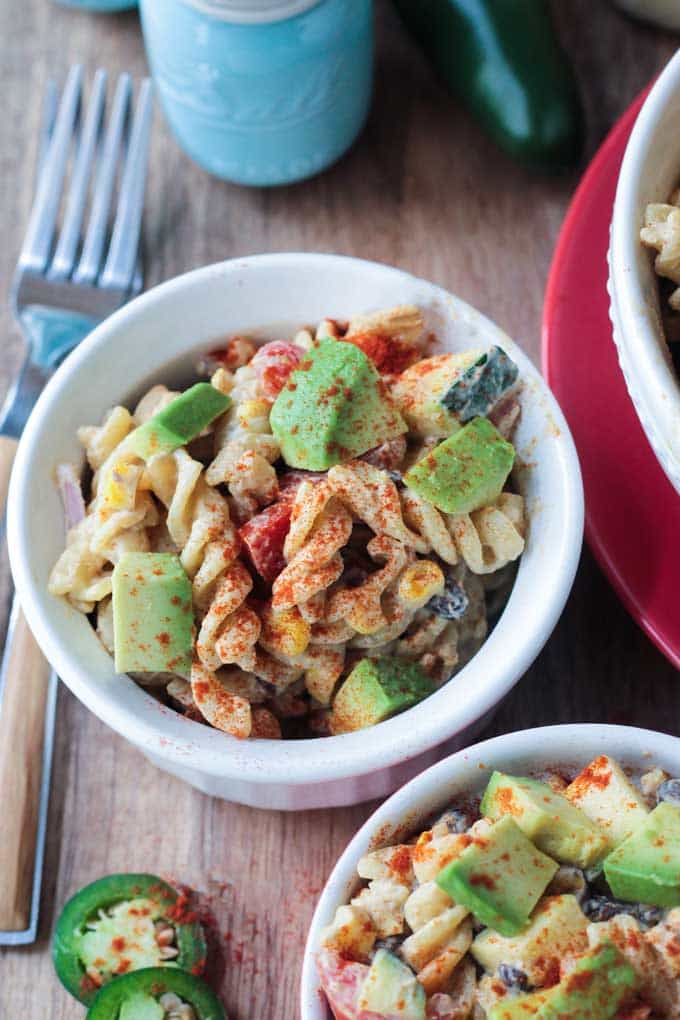 Southwest Black Bean Pasta Salad in a small white bowl. A wooden handled fork lies next to the bowl. Blue salt shaker behind.