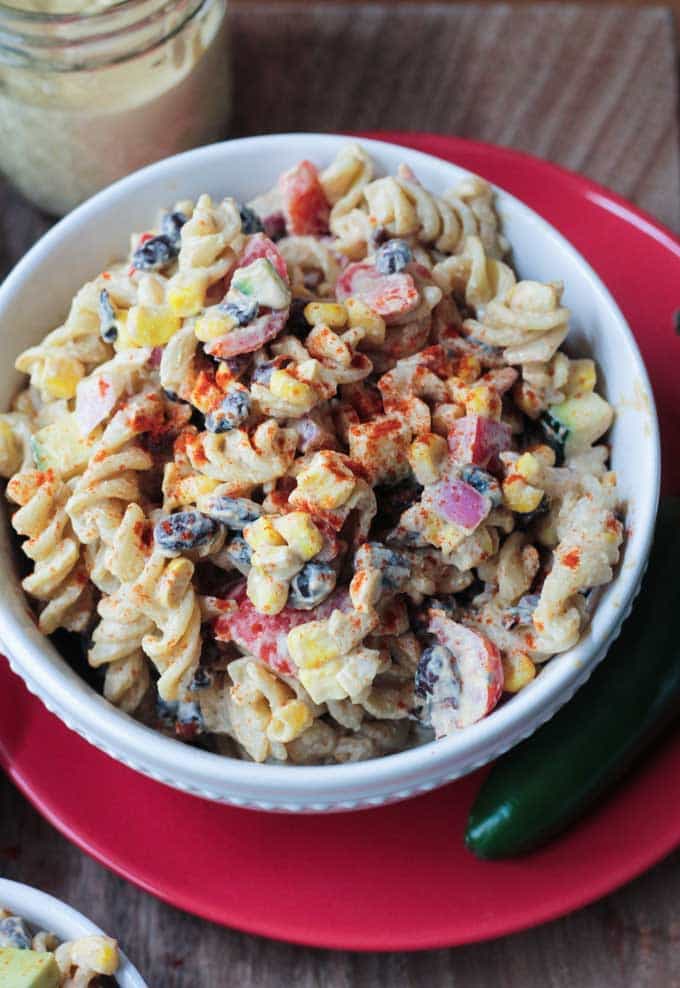 Southwest Black Bean Pasta Salad in a white bowl on a red plate. One jalapeño on the plate next to the bowl.