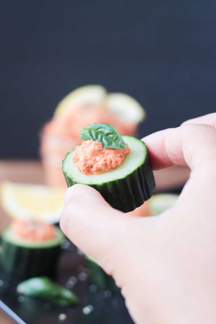 Hand holding one cucumber slice with sun dried tomato spread