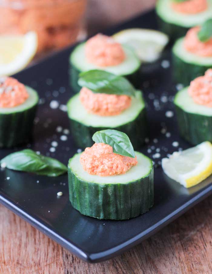 Slice of cucumber topped with sun dried tomato dip and topped with a small fresh basil leaf.