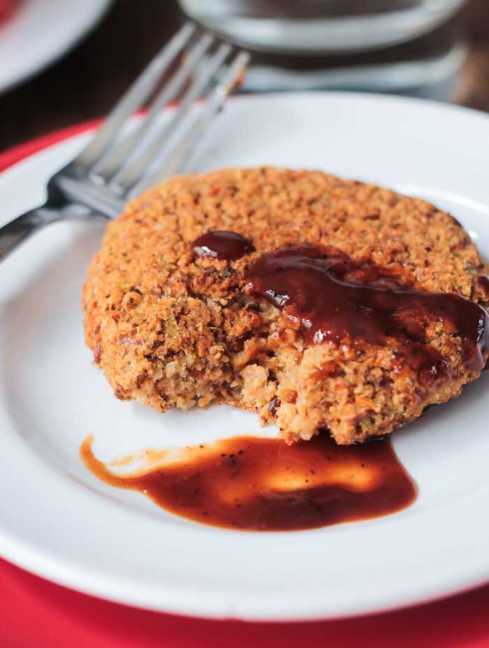Pinto bean patty on a white plate with BBQ sauce and a fork.