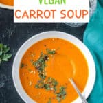 Carrot soup in a white bowl with a spoon and herb garnish.