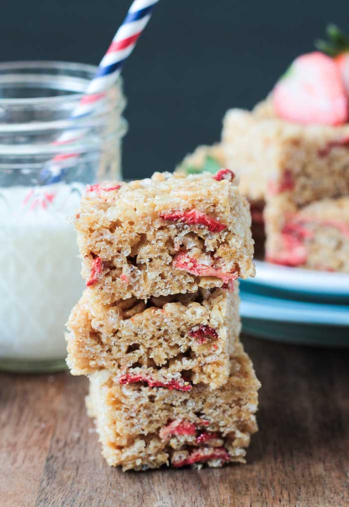 Stack of Brown Rice Crispy Treats w Strawberries. Plate of more treats in the background with fresh strawberries.