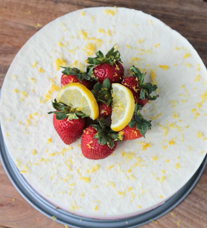 Strawberry Lemonade Ice Cream Cake w/ Pretzel Pecan Crust - this beautiful frozen dessert is easily made with So Delicious Dairy Free Simply Strawberry and a few extra ingredients. Sweet, tart, and gluten free! You' re gonna love this summer vegan ice cream cake! Overhead view of Strawberry Lemonade Ice Cream Cake garnished with fresh strawberries, lemon slices, and lemon zest!
