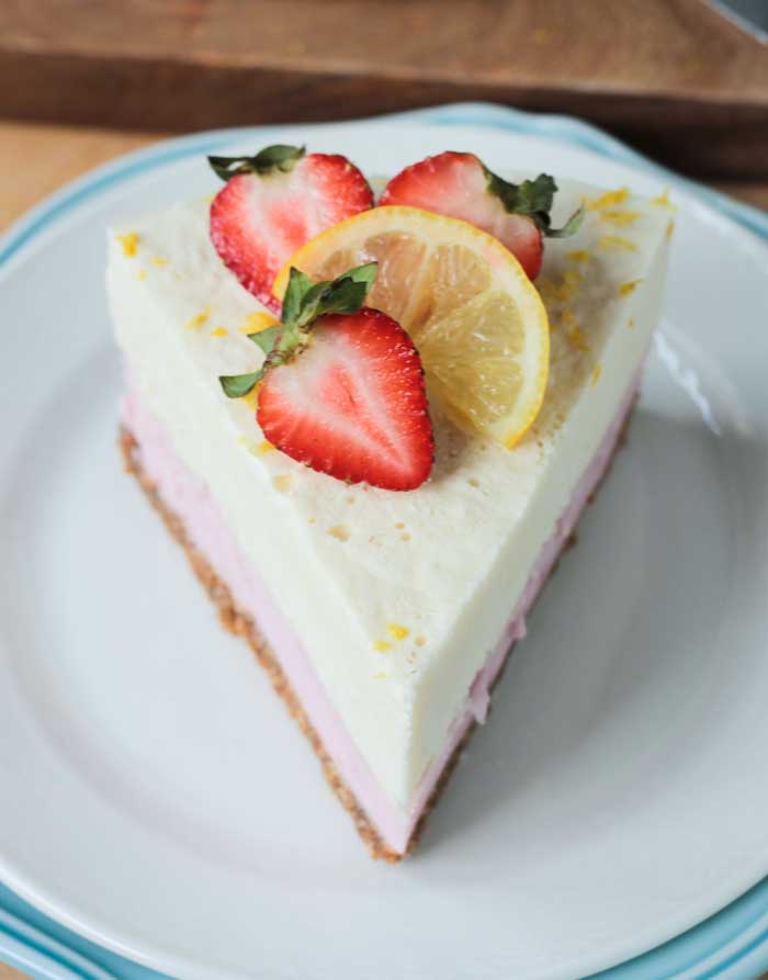 One slice of Strawberry Lemonade Ice Cream Cake garnished with fresh strawberries and a lemon slice.