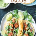 Two tacos filled with baked tofu, shredded cabbage, cilantro, and avocado sauce.
