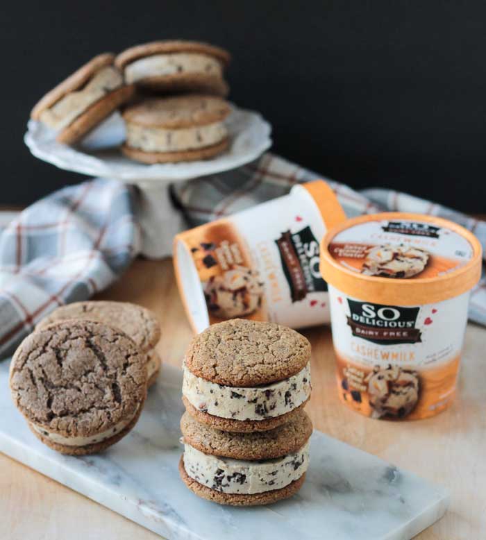 Pile of sugar cookie ice cream sandwiches on a marble slab. Two pints of So Delicious Cashew Milk ice cream behind.