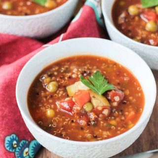 Chunky vegetable quinoa soup in a white bowl.