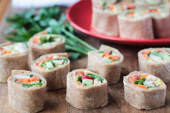 Tortilla Rollups w/ Dairy Free Veggie Cream Cheese - These creamy, crunchy little bites are the perfect appetizer or lunch. Loaded with dairy free veggie cream cheese, then topped with more fresh cut veggies, and all rolled up into a tortilla and cut into bite size pieces - these are not only delicious, but so fun to eat! Perfect for your child's lunchbox - customize it with their favorite veggies. Tray full of veggie tortilla roll ups.
