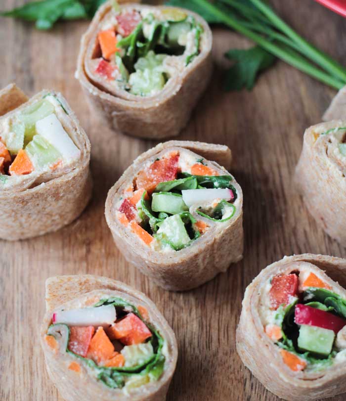 Bite size tortilla rollups with cucumber, red pepper, carrot, and cream cheese on a wooden board.