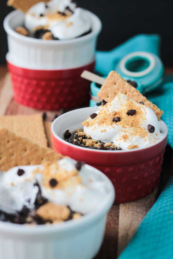 Two bowls of s'mores pudding - white bowl in front, red bowl behind. Two more stacked bowls behind - red one on bottom is empty, white one on top also filled with pudding.