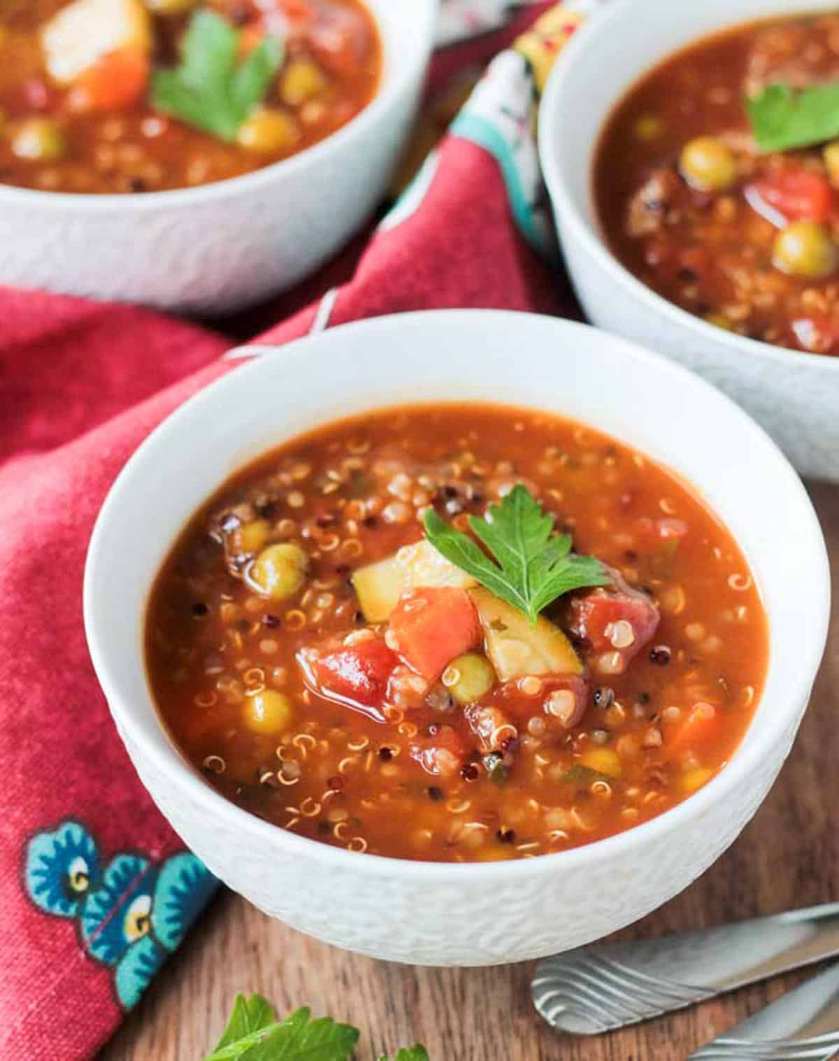 Bowl of quinoa vegetable soup garnished with a fresh sprig of parsley.