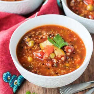 Bowl of quinoa vegetable soup garnished with a fresh sprig of parsley.