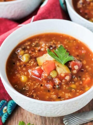 Bowl of quinoa vegetable soup garnished with a fresh sprig of parsley.