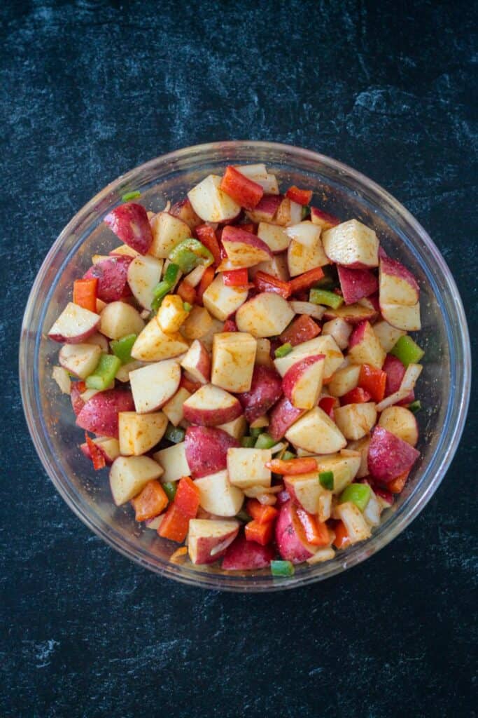 Diced potatoes, peppers, and onions mixed with spices in a bowl.
